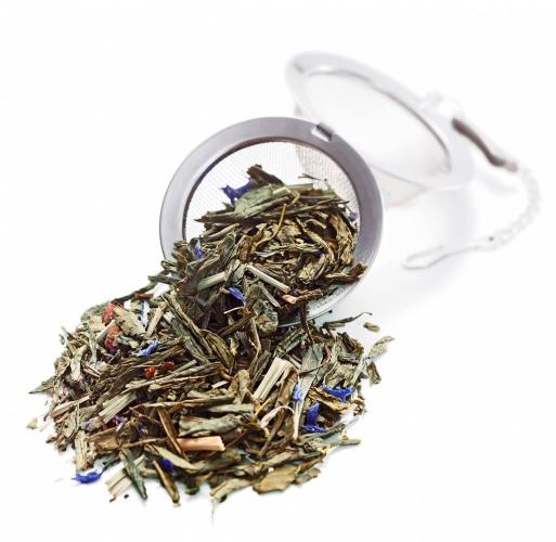 Nahaufnahme eines Teesiebs mit losem Grüntee und blauen Blüten auf weißem Hintergrund