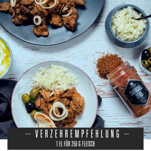Teller mit gewürztem Fleisch, Zwiebeln, Oliven und Beilagen, daneben ein Gewürzglas
