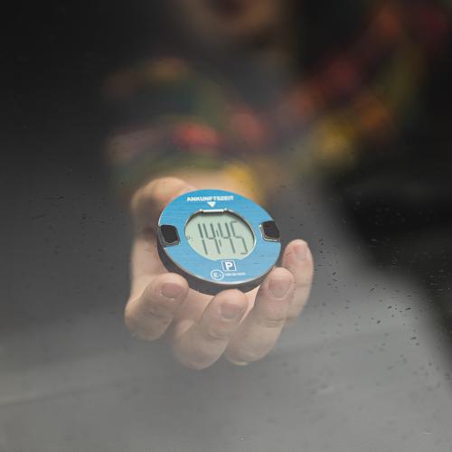 Nahaufnahme einer digitalen Parkscheibe, die von einer Hand gehalten wird, sichtbar durch eine Autoscheibe.