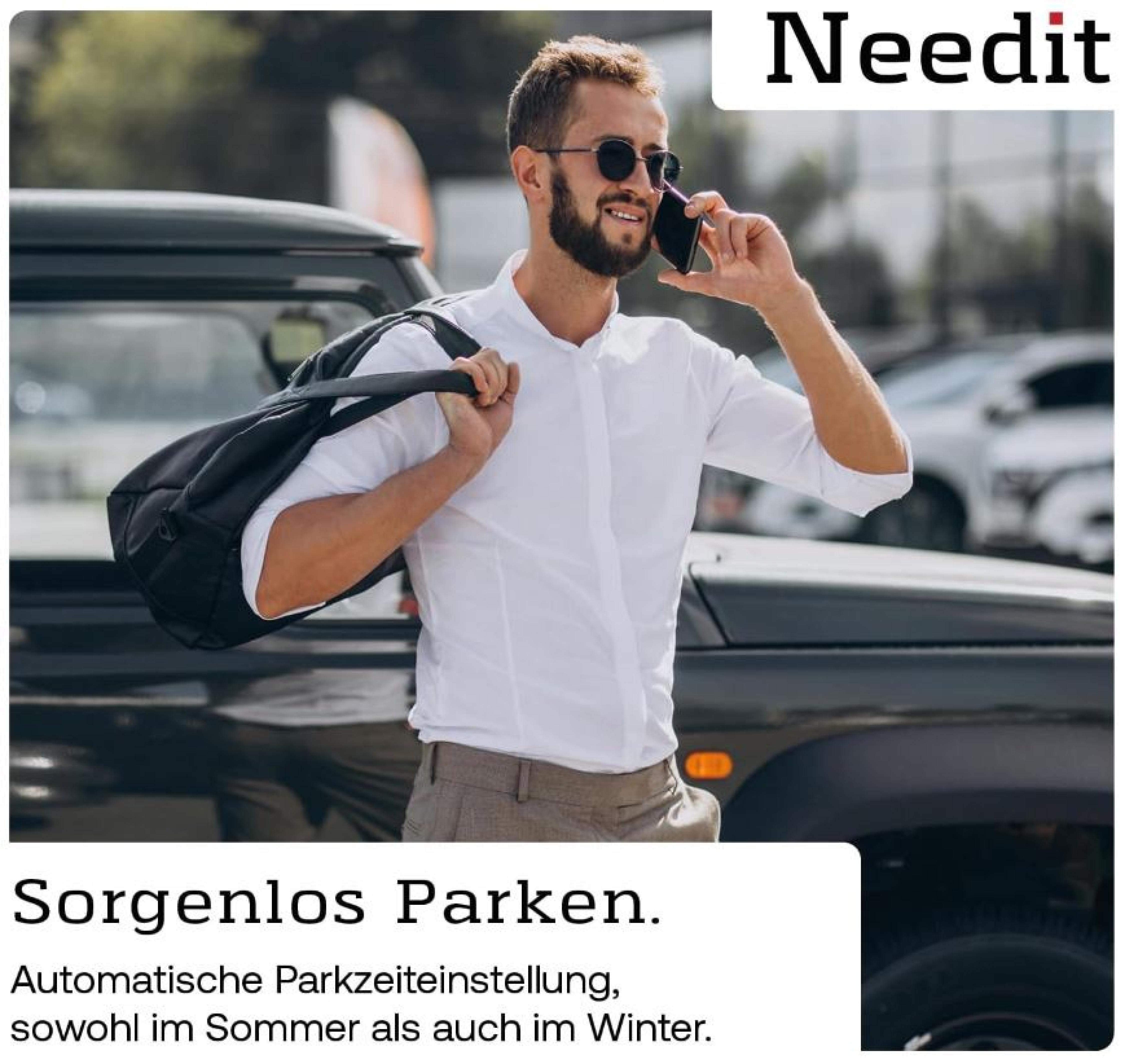 Mann mit Sonnenbrille und Tasche steht neben einem Auto und telefoniert