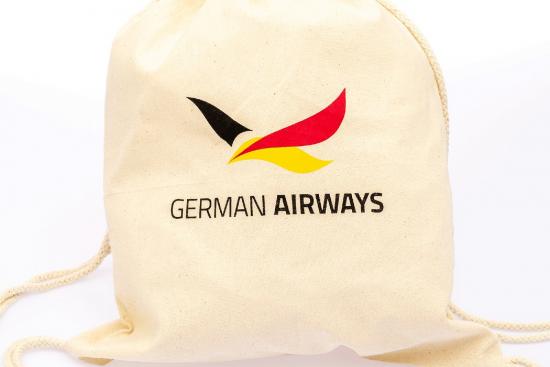 Beiger Turnbeutel mit dem Logo von German Airways, bestehend aus einem stilisierten Vogel in den Farben Schwarz, Rot und Gelb.