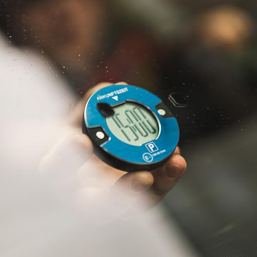 Nahaufnahme einer blauen elektronischen Parkscheibe, die in einer Hand gehalten wird und die Ankunftszeit anzeigt.