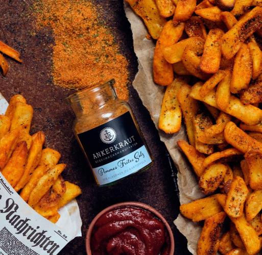 Ein Glas Ankerkraut Pommes Frites Salz neben goldbraun gebackenen Pommes und einer Schale Ketchup