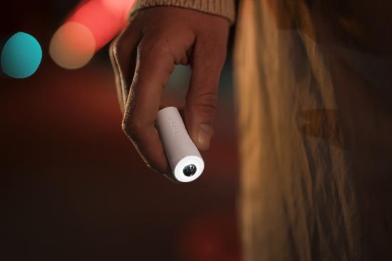 Eine Person hält eine kleine, tragbare LED-Taschenlampe in der Hand, abgebildet bei Nacht mit unscharfem, buntem Hintergrundlicht.