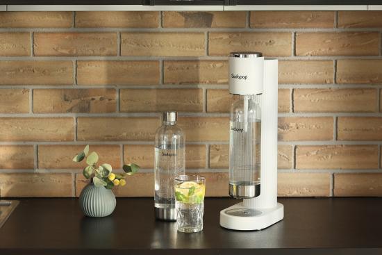 Wassersprudler neben Glas mit Limetten und Karaffe auf Küchenarbeitsplatte