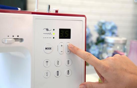 Nahaufnahme einer Hand, die ein digitales Bedienfeld einer Nähmaschine einstellt