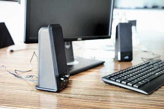 Arbeitsplatz mit Monitor, Lautsprechern und Tastatur auf einem Holztisch