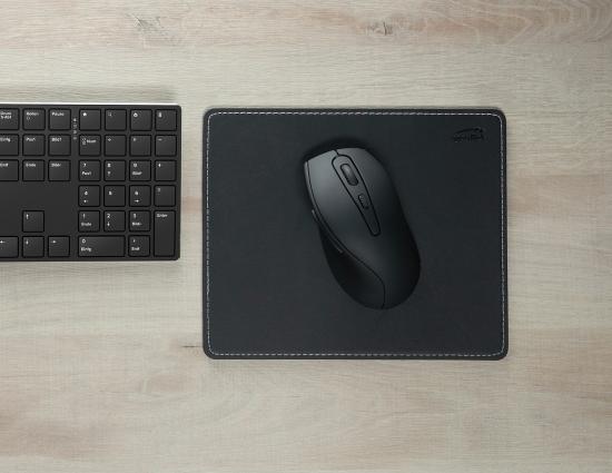 Schwarze ergonomische Maus auf einem Mousepad neben einer schwarzen Tastatur auf einem Holztisch