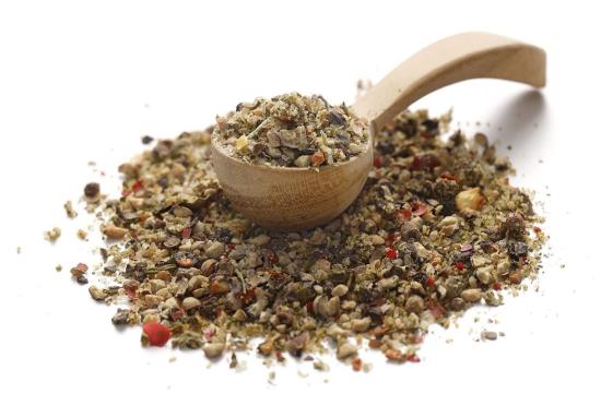 Ein Holzlöffel gefüllt mit einer bunten Gewürzmischung, gestützt auf einem Haufen Kräuter und Gewürze.