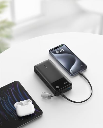 Moderner Tisch mit Smartphone, Powerbank und kabellosen Ohrhörern Ein Tisch mit einem Smartphone, das an eine Powerbank angeschlossen ist, kabellose Ohrhörer und ein Laptop